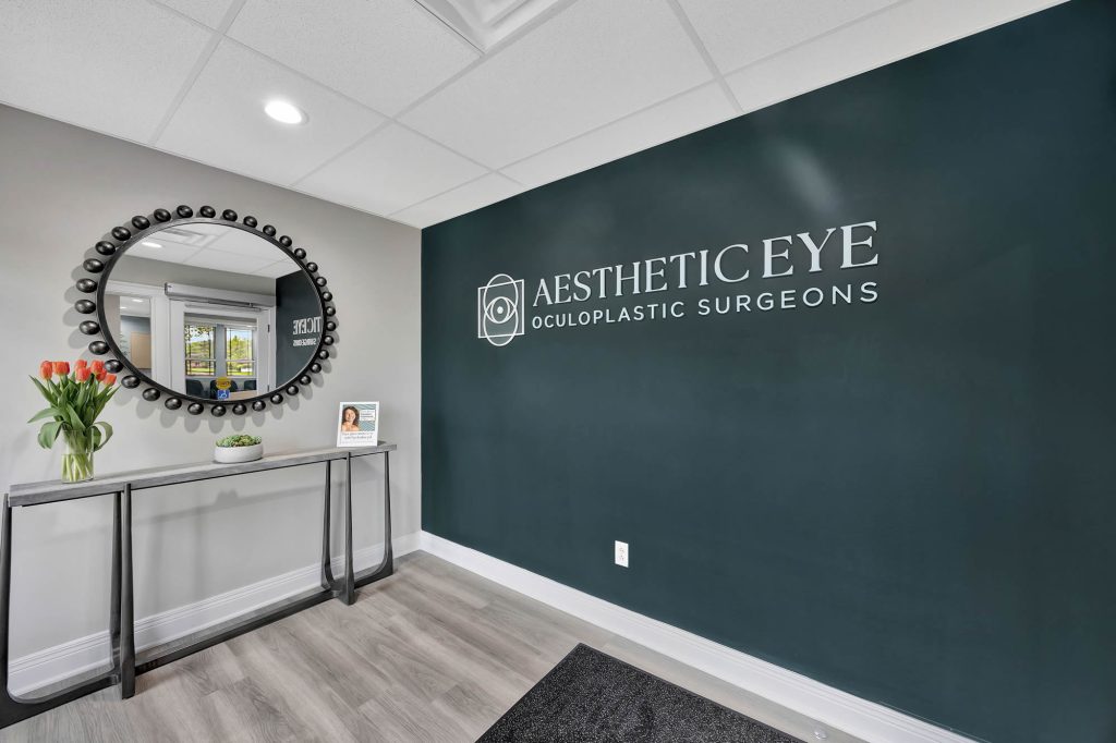 Aesthetic Eye logo on a teal wall next to a round mirror and console.