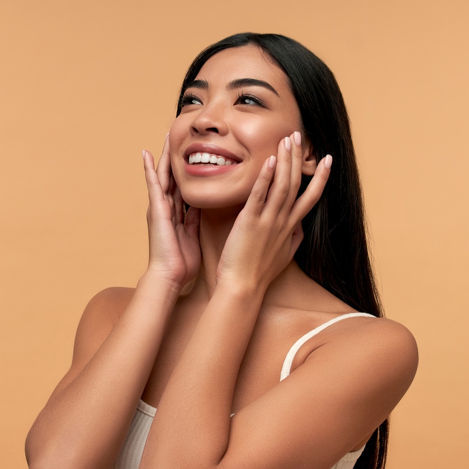 Young Asian woman with clean healthy glowing skin in white top isolated on beige background. Facial skin care concept, spa, cosmetology, plastic surgery.