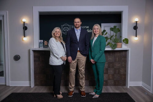 Three professionals standing in front of a reception desk with the logo for Preserve Vision Group.
