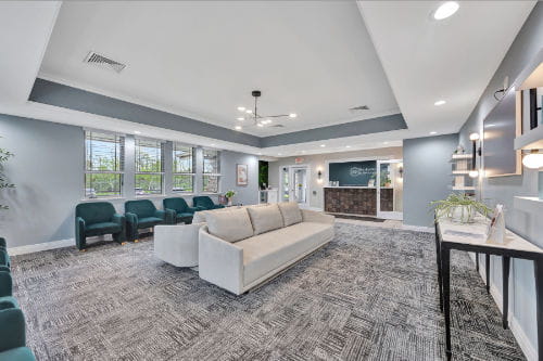 A modern office reception area featuring a light-colored sofa, dark chairs, and a front desk in the background.